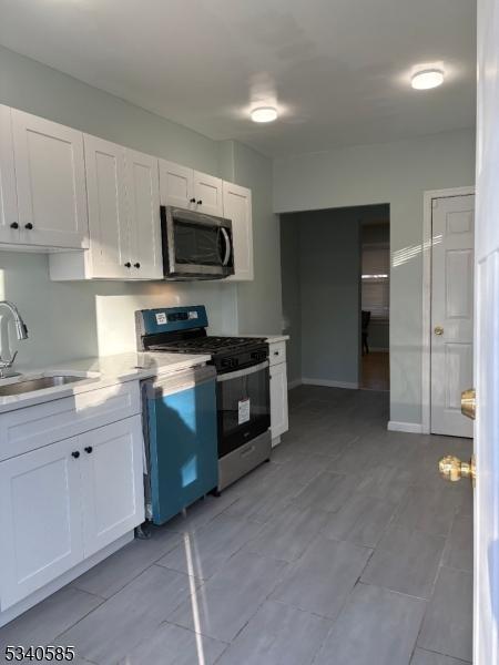 kitchen featuring baseboards, a sink, light countertops, white cabinets, and appliances with stainless steel finishes