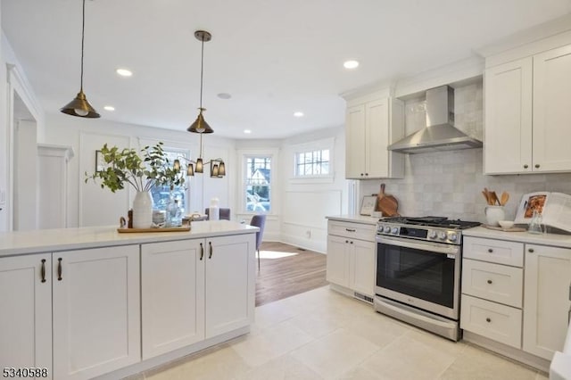 kitchen featuring white cabinetry, light countertops, wall chimney range hood, gas stove, and pendant lighting