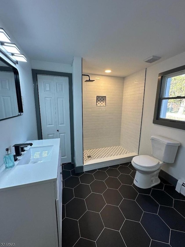 bathroom featuring a tile shower, visible vents, toilet, and vanity