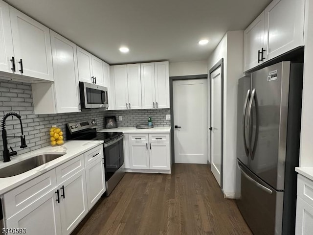 kitchen featuring dark wood-style flooring, a sink, stainless steel appliances, white cabinetry, and tasteful backsplash