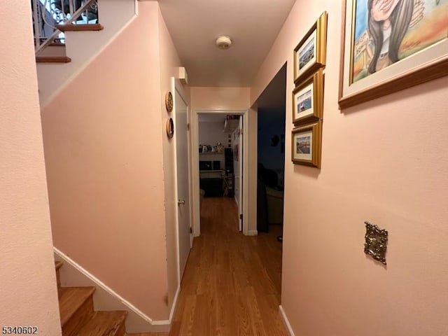 corridor with stairway, wood finished floors, and baseboards