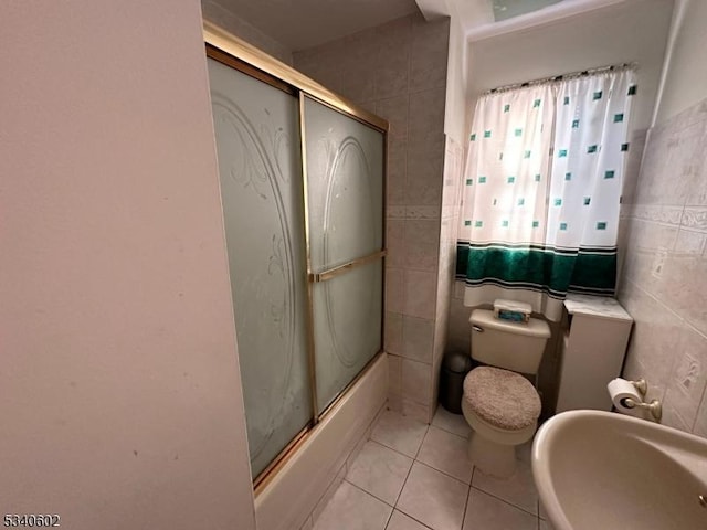 bathroom featuring toilet, shower / bath combination with glass door, tile patterned flooring, and tile walls