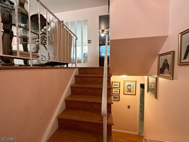 staircase featuring wood finished floors, a ceiling fan, and baseboards