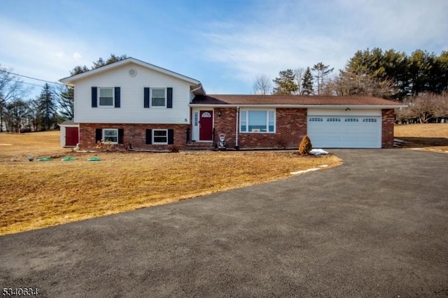 split level home featuring a garage, a front yard, brick siding, and aphalt driveway