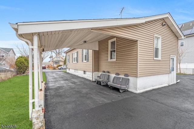 exterior space featuring an attached carport, a front lawn, and aphalt driveway