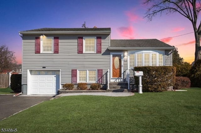 split level home featuring aphalt driveway, a garage, and a front lawn