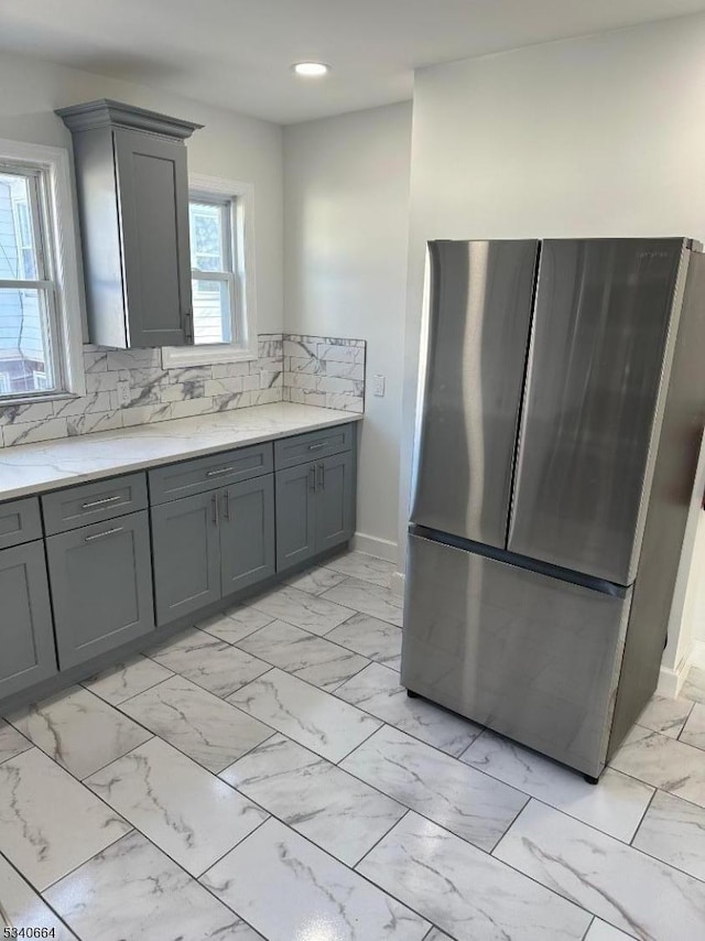 kitchen featuring tasteful backsplash, freestanding refrigerator, gray cabinets, and marble finish floor