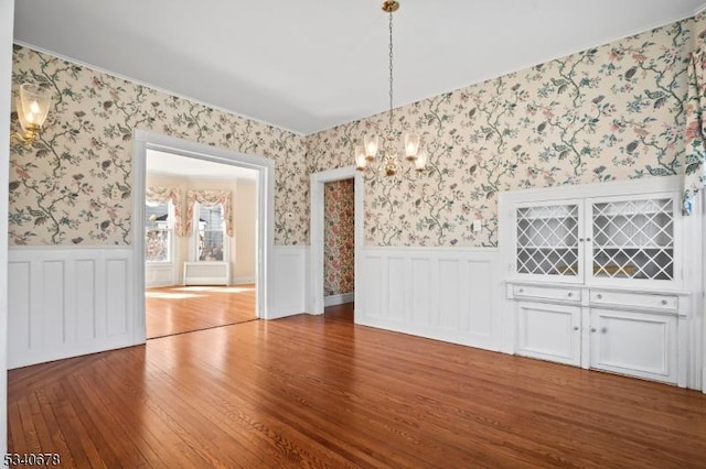 unfurnished dining area featuring wood finished floors, wainscoting, a notable chandelier, and wallpapered walls