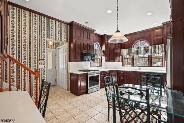 kitchen featuring stainless steel gas stove, hanging light fixtures, light countertops, black microwave, and a sink