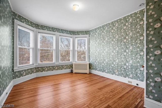 empty room with baseboards, radiator heating unit, wood-type flooring, and wallpapered walls