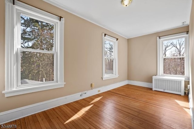 spare room featuring baseboards, radiator heating unit, wood-type flooring, and a healthy amount of sunlight