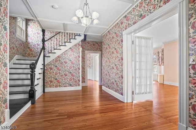 entrance foyer featuring wallpapered walls, an inviting chandelier, wood finished floors, baseboards, and stairs