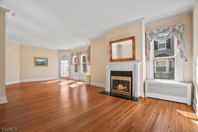 unfurnished living room featuring crown molding, radiator, a fireplace with flush hearth, wood finished floors, and baseboards