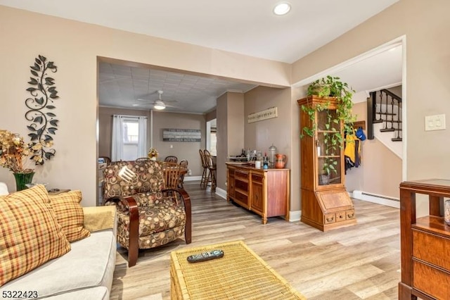 living area featuring ceiling fan, a baseboard heating unit, baseboards, stairs, and light wood-style floors