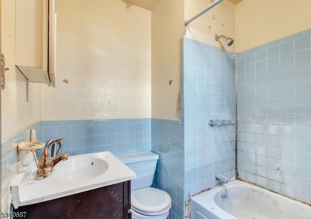 bathroom featuring tile walls, shower / bathtub combination, toilet, wainscoting, and vanity