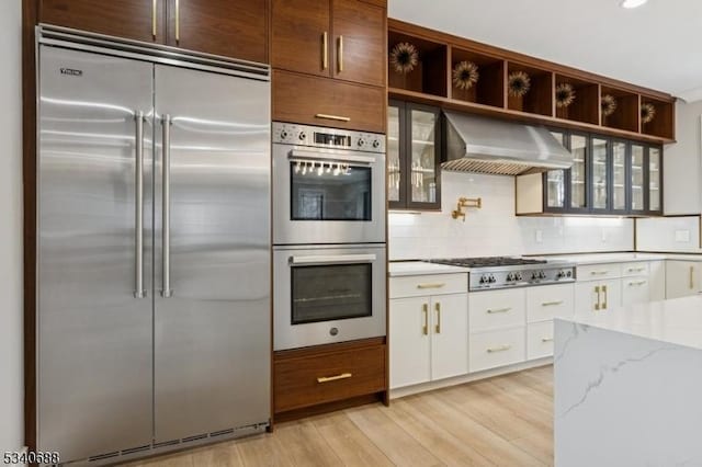 kitchen featuring open shelves, white cabinets, appliances with stainless steel finishes, light wood-type flooring, and wall chimney exhaust hood