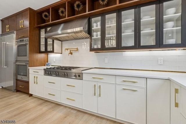 kitchen with stainless steel appliances, extractor fan, light countertops, and light wood-style flooring