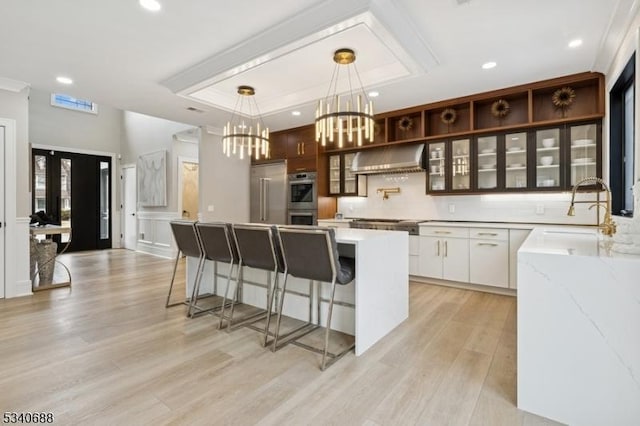 kitchen with stainless steel appliances, a sink, ventilation hood, light wood-type flooring, and a kitchen bar