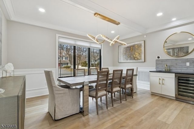 dining area featuring beverage cooler, a wainscoted wall, ornamental molding, light wood finished floors, and beamed ceiling