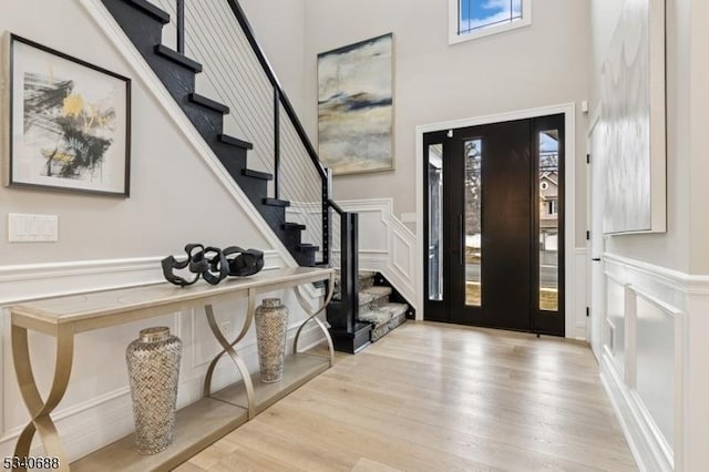 foyer with stairway, wainscoting, wood finished floors, and a decorative wall