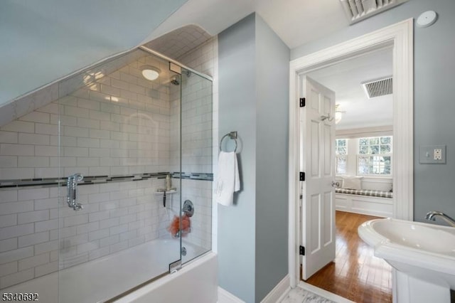 bathroom featuring bath / shower combo with glass door, visible vents, a sink, wood finished floors, and baseboards