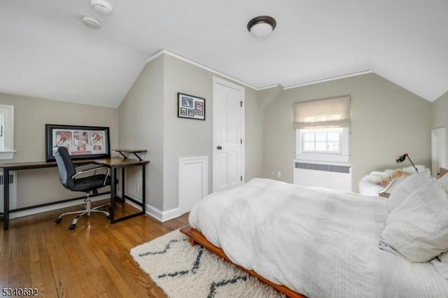 bedroom featuring radiator, baseboards, wood finished floors, and lofted ceiling