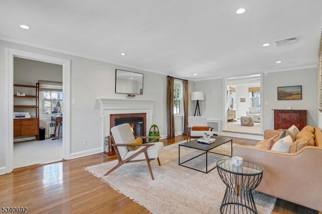 living area with a fireplace, visible vents, crown molding, and wood finished floors