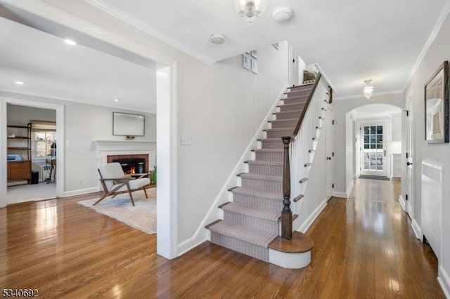 stairway featuring arched walkways, a brick fireplace, hardwood / wood-style flooring, and crown molding