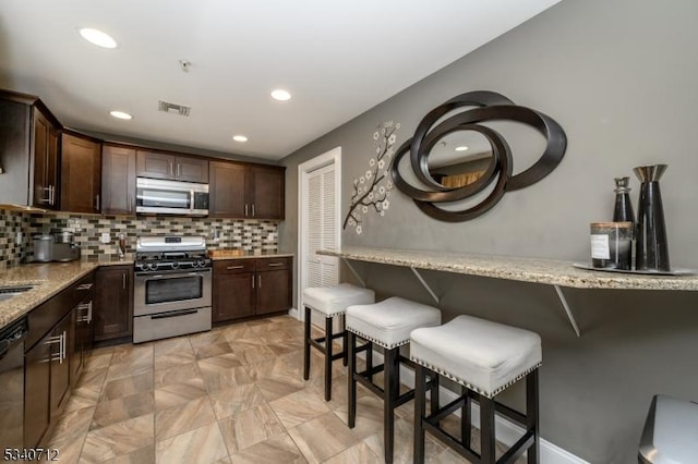 kitchen with stainless steel appliances, a breakfast bar area, visible vents, and dark brown cabinetry