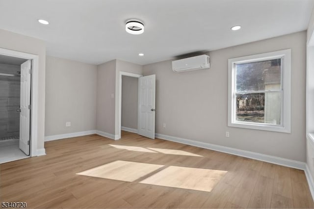 unfurnished bedroom featuring light wood-style flooring, baseboards, and an AC wall unit