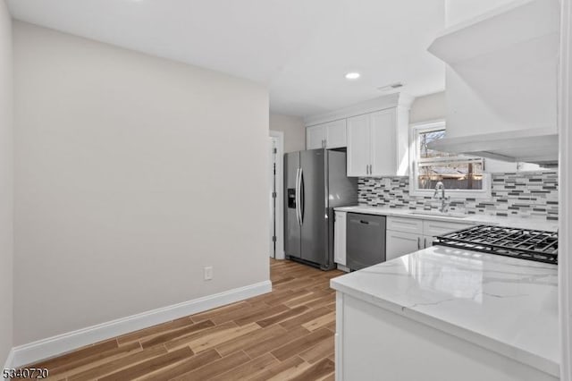 kitchen with light wood-style flooring, stainless steel appliances, a sink, white cabinetry, and backsplash