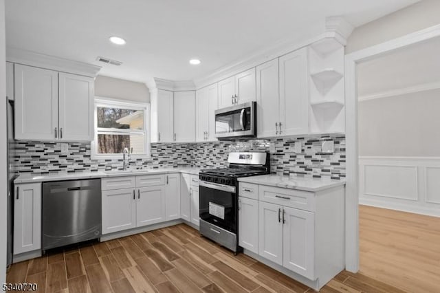 kitchen with appliances with stainless steel finishes, wood finished floors, light countertops, open shelves, and a sink