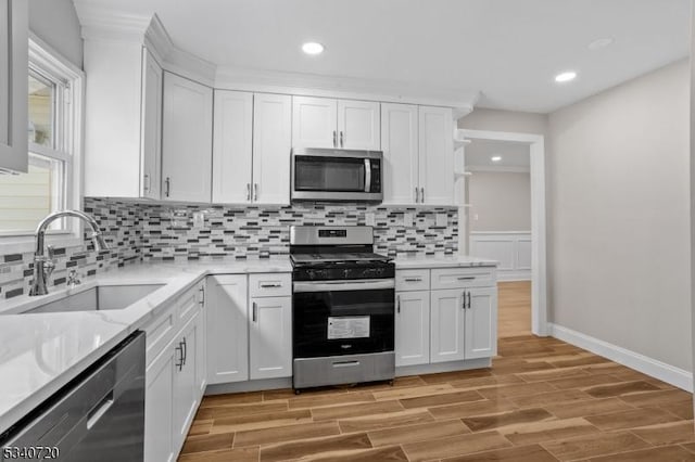 kitchen with appliances with stainless steel finishes, white cabinetry, a sink, and light wood finished floors