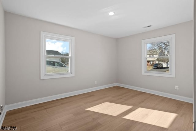 empty room featuring a healthy amount of sunlight, visible vents, baseboards, and wood finished floors