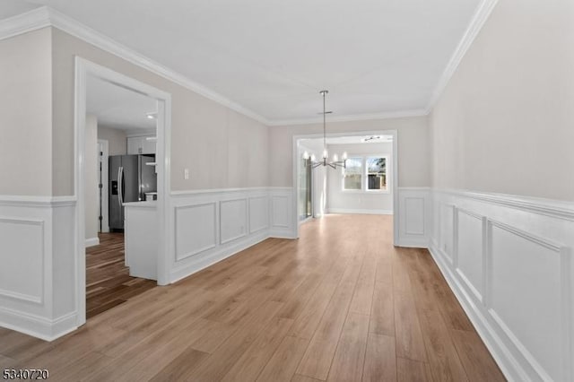 unfurnished dining area featuring a wainscoted wall, a decorative wall, an inviting chandelier, ornamental molding, and light wood-type flooring