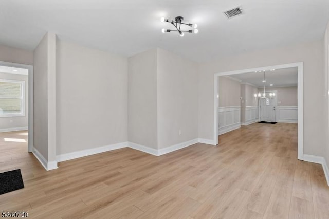 spare room featuring baseboards, light wood finished floors, visible vents, and an inviting chandelier