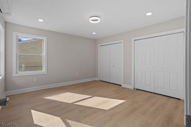 unfurnished bedroom featuring baseboards, light wood-style floors, recessed lighting, and multiple closets