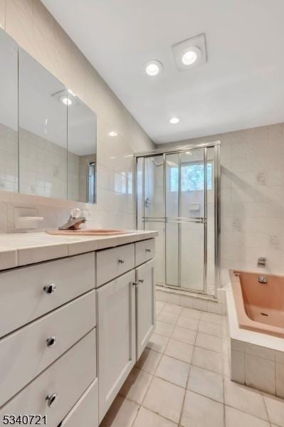 bathroom with a stall shower, tile patterned floors, a whirlpool tub, vanity, and tile walls