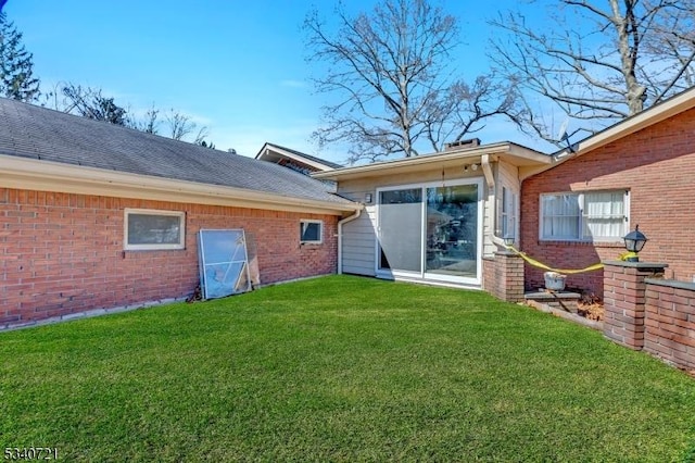 rear view of property featuring a yard, brick siding, and a shingled roof