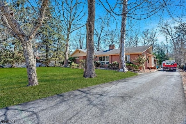 ranch-style home featuring a front yard, driveway, a chimney, and brick siding