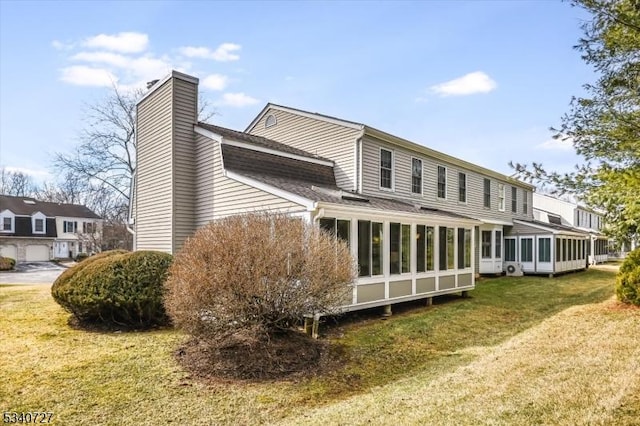 rear view of house with a shingled roof, a sunroom, a yard, and a chimney