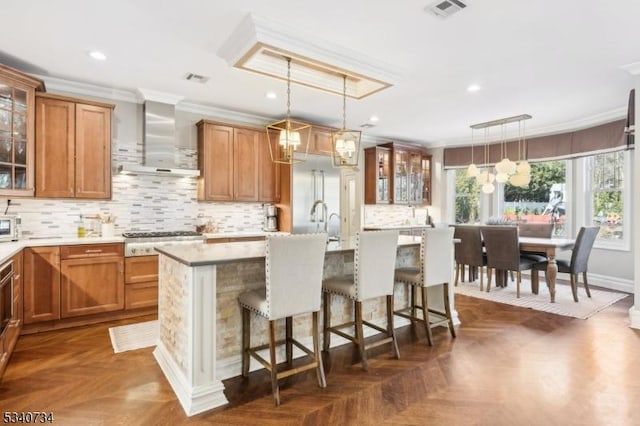 kitchen featuring visible vents, brown cabinets, crown molding, wall chimney range hood, and stainless steel gas cooktop