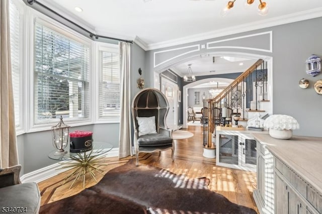 living area featuring arched walkways, a notable chandelier, wood finished floors, ornamental molding, and stairway