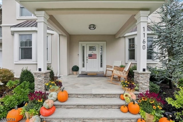 property entrance with a standing seam roof, covered porch, metal roof, and stucco siding