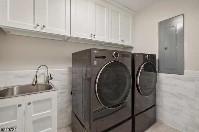 laundry area with a sink, tile walls, cabinet space, electric panel, and washing machine and clothes dryer