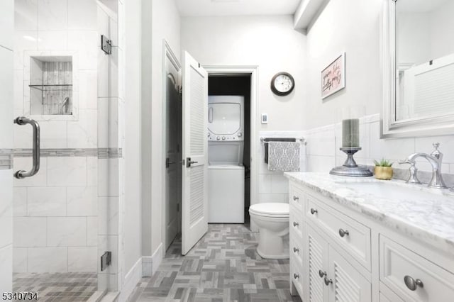 full bathroom featuring toilet, vanity, tile walls, stacked washing maching and dryer, and a stall shower