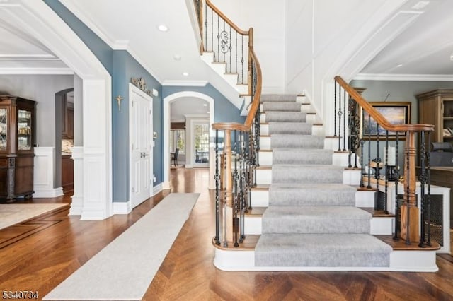 stairs with ornamental molding, arched walkways, recessed lighting, and parquet flooring