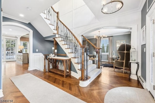 foyer entrance with arched walkways, crown molding, a decorative wall, baseboard heating, and a chandelier