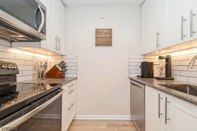 kitchen with stainless steel appliances, a sink, white cabinetry, baseboards, and dark stone countertops