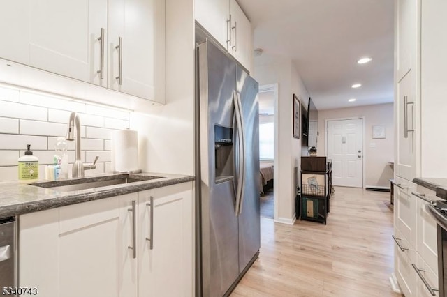 kitchen featuring stainless steel appliances, white cabinetry, a sink, and light wood-style flooring